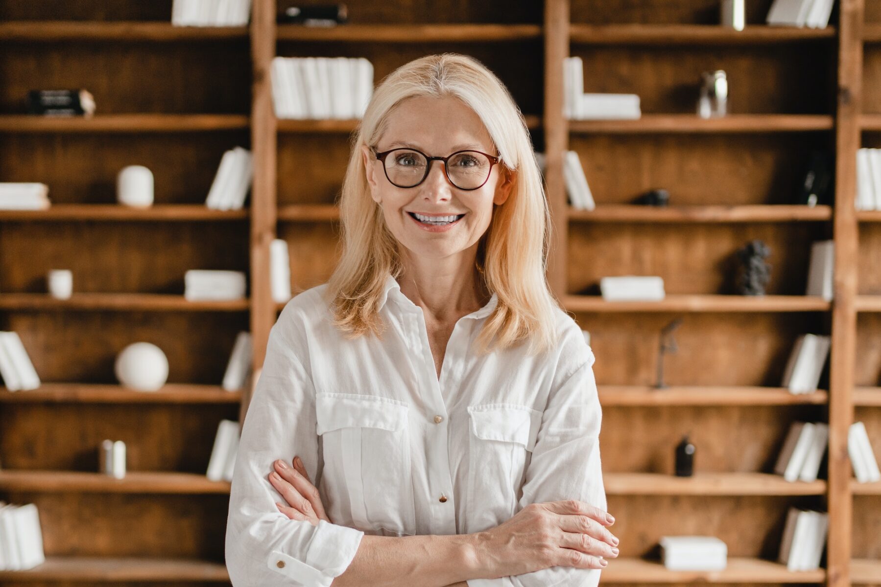 Businesswoman librarian psychologist teacher with arms crossed looking at camera in library office
